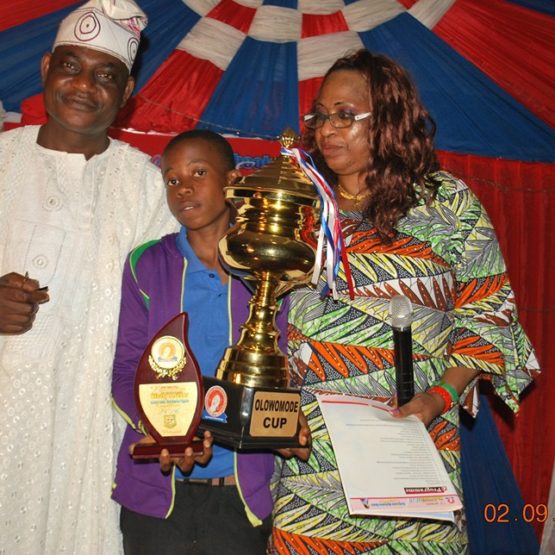 Chief Matthew Ogunyeye presenting the Olowomode Cup he donated to the winner of a student competition organized by the Igogo Daughters Association